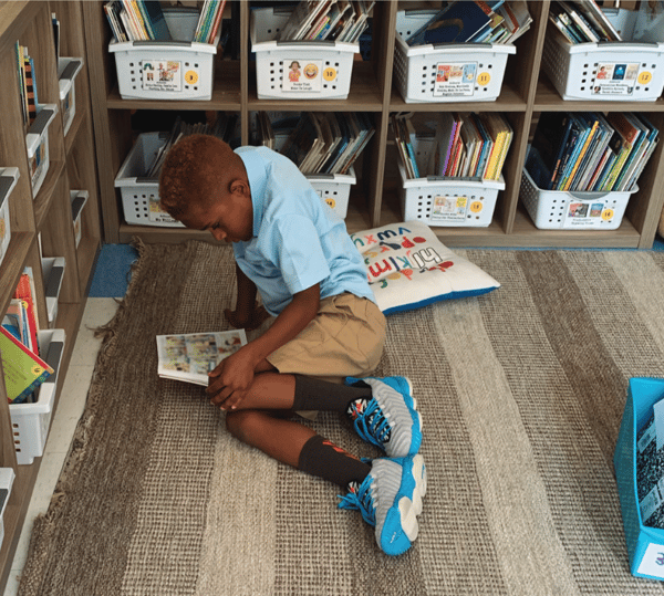 Student Reading on Classroom Floor surrounded by bins filled with books