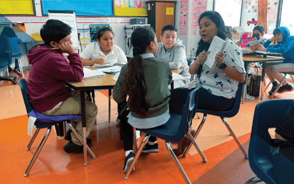 Whispering in the Wind Book Photo of Teacher talking  at Table with Students Listening